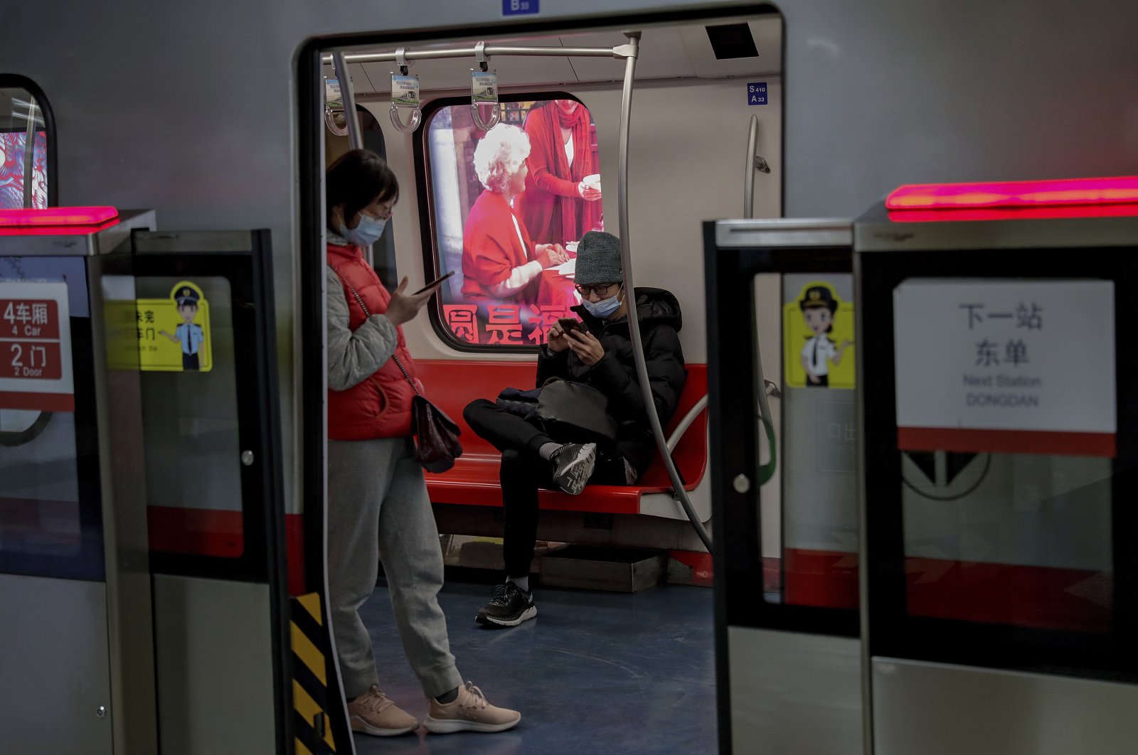 Commuters wearing face masks to help curb the spread of the coronavirus browse their smartphones inside a subway train in Beijing, China, Feb. 10, 2021. (AP Photo)