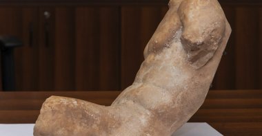 A 5th century B.C. statue about 37 centimeters (14.5 inches), depicting a seated young man who slightly reclines, can be seen, Athens, Greece, March 19, 2021. (Greek Police via AP)