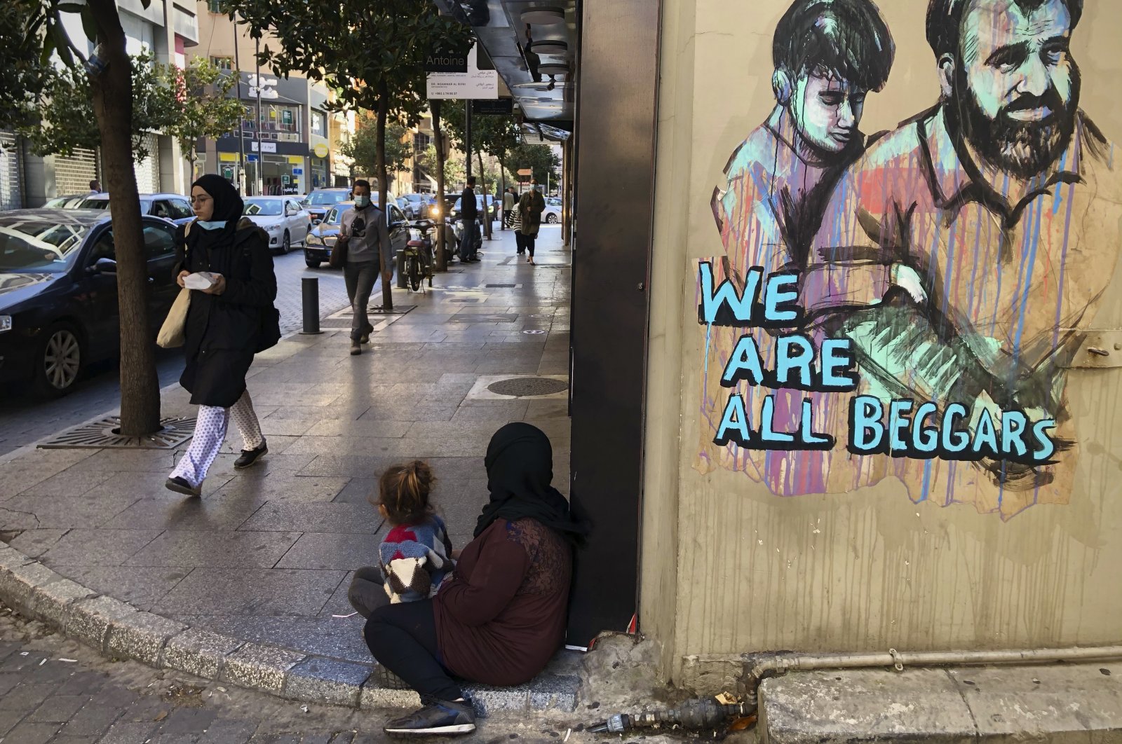 Passersby walk by a woman (center) sitting on the ground with her daughter begging on Beirut's commercial Hamra Street, in Beirut, Lebanon, March 16, 2021. (AP Photo)