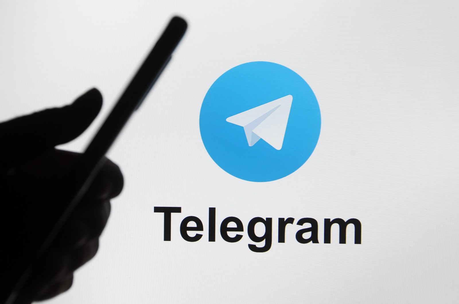 Telegram logo is seen on a screen behind the silhouette of a hand holding a mobile phone, Kyiv, Ukraine, Jan. 12, 2021. (Reuters Photo)
