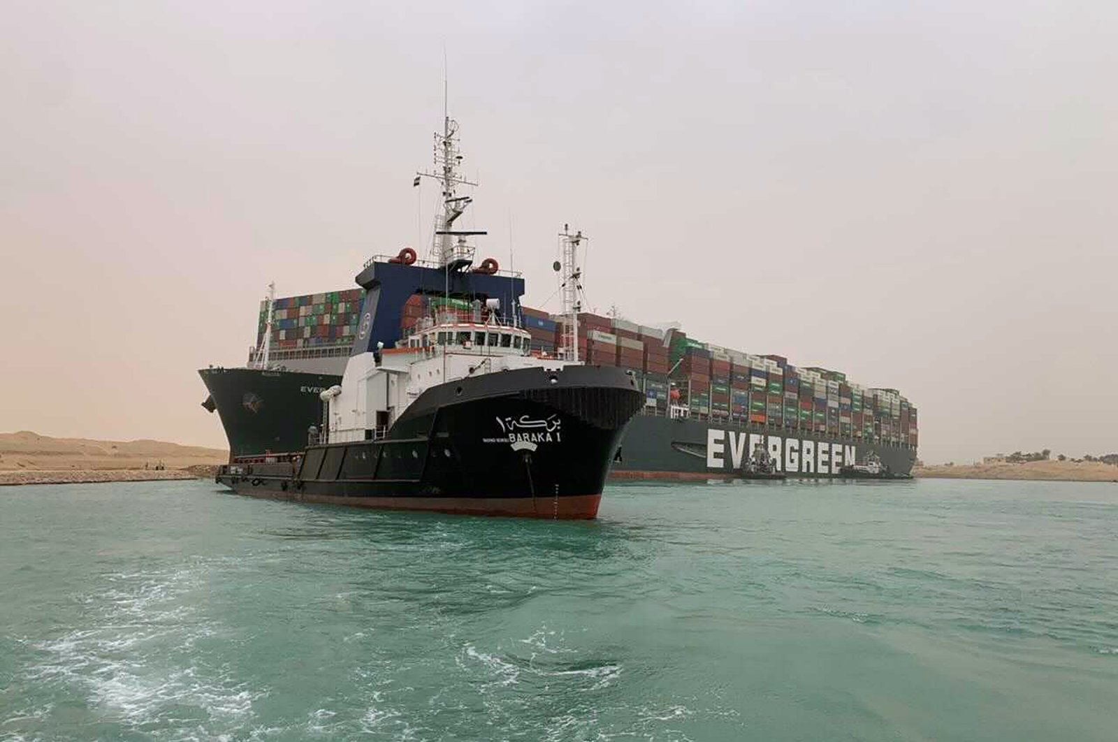 In this photo released by the Suez Canal Authority, a boat navigates in front of a massive cargo ship, named the Ever Green, rear, sits grounded Wednesday, March 24, 2021, after it turned sideways in Egypt’s Suez Canal. (Suez Canal Authority via AP)
