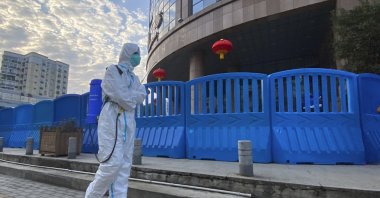 A worker in protective overalls and carrying disinfecting equipment walks outside the Wuhan Central Hospital in Wuhan, central China, Feb. 6, 2021. (AP Photo)