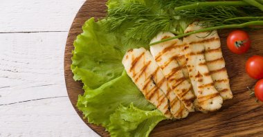 Slices of grilled halloumi cheese with green salad, fresh herbs and tomatoes. (Shutterstock Photo)