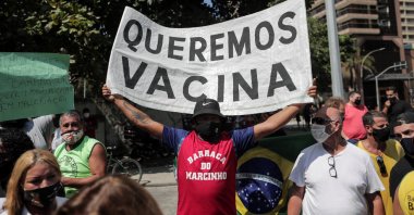 A man holds up a banner calling for a vaccine against COVID-19 during protests against the new measures implemented to stop its spread, on the beach of Copacabana, in Rio de Janeiro, Brazil, March 26, 2021.  (EPA Photo)