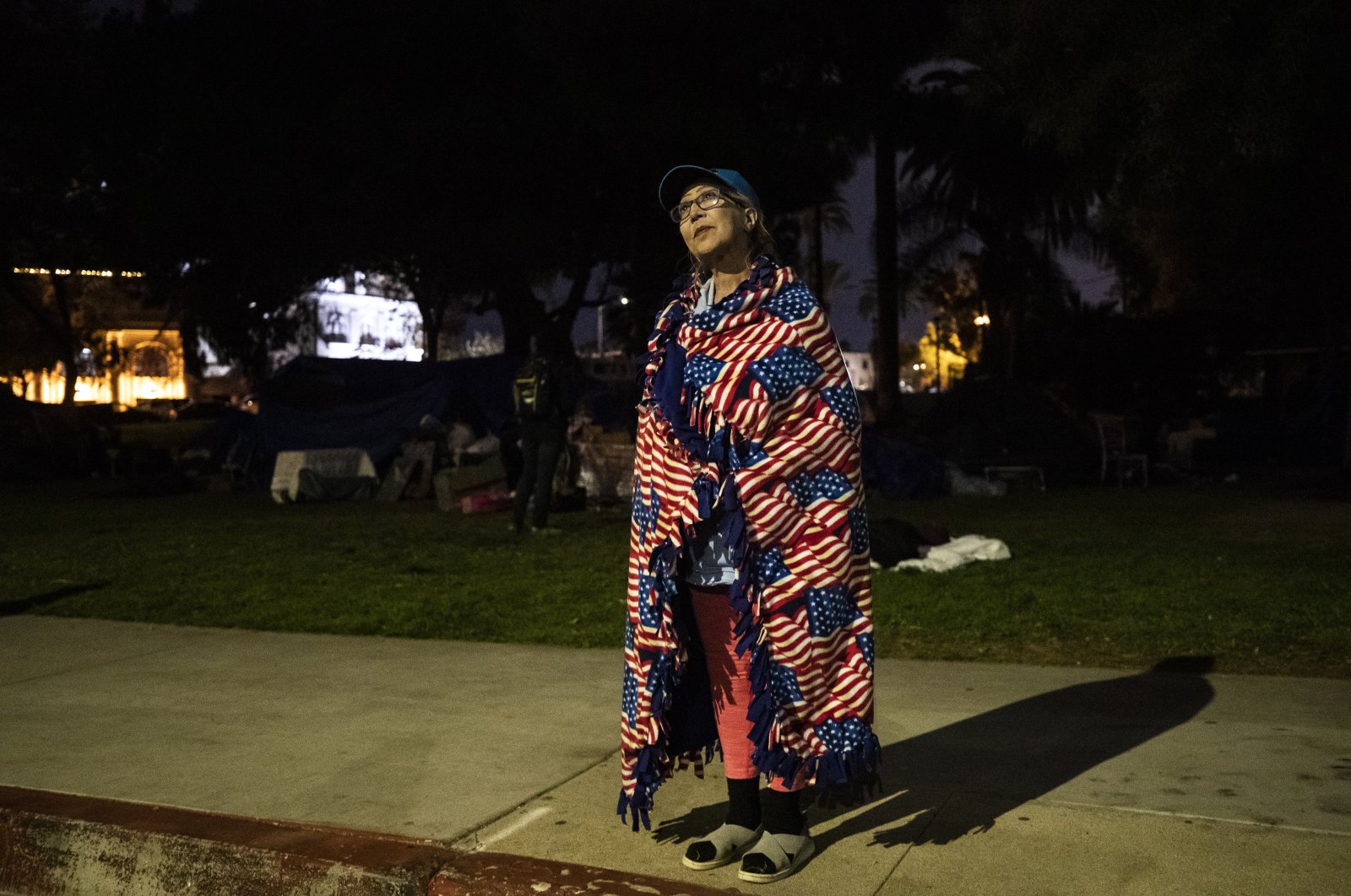 Antonia Ramirez from Mexico, experiencing homelessness for the past 20 years, stands wrapped in a blanket displaying American flags next to the tents of the homeless encampment of Echo Park Lake as a large police force is mobilized to clear the area in Los Angeles, California, U.S., March 24, 2021. (EPA Photo)