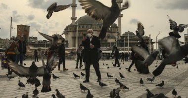 A man feeds pigeons amid the coronavirus pandemic, at Taksim Square, Istanbul, Turkey, March 25, 2021. (AP Photo)