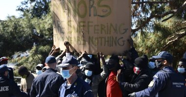 Police stand in front of protesting migrants during the visit of EU Commissioner Ylva Johansson at a refugee camp in the port of Vathy on the eastern Aegean island of Samos, Greece, Monday, March 29, 2021. (AP Photo)
