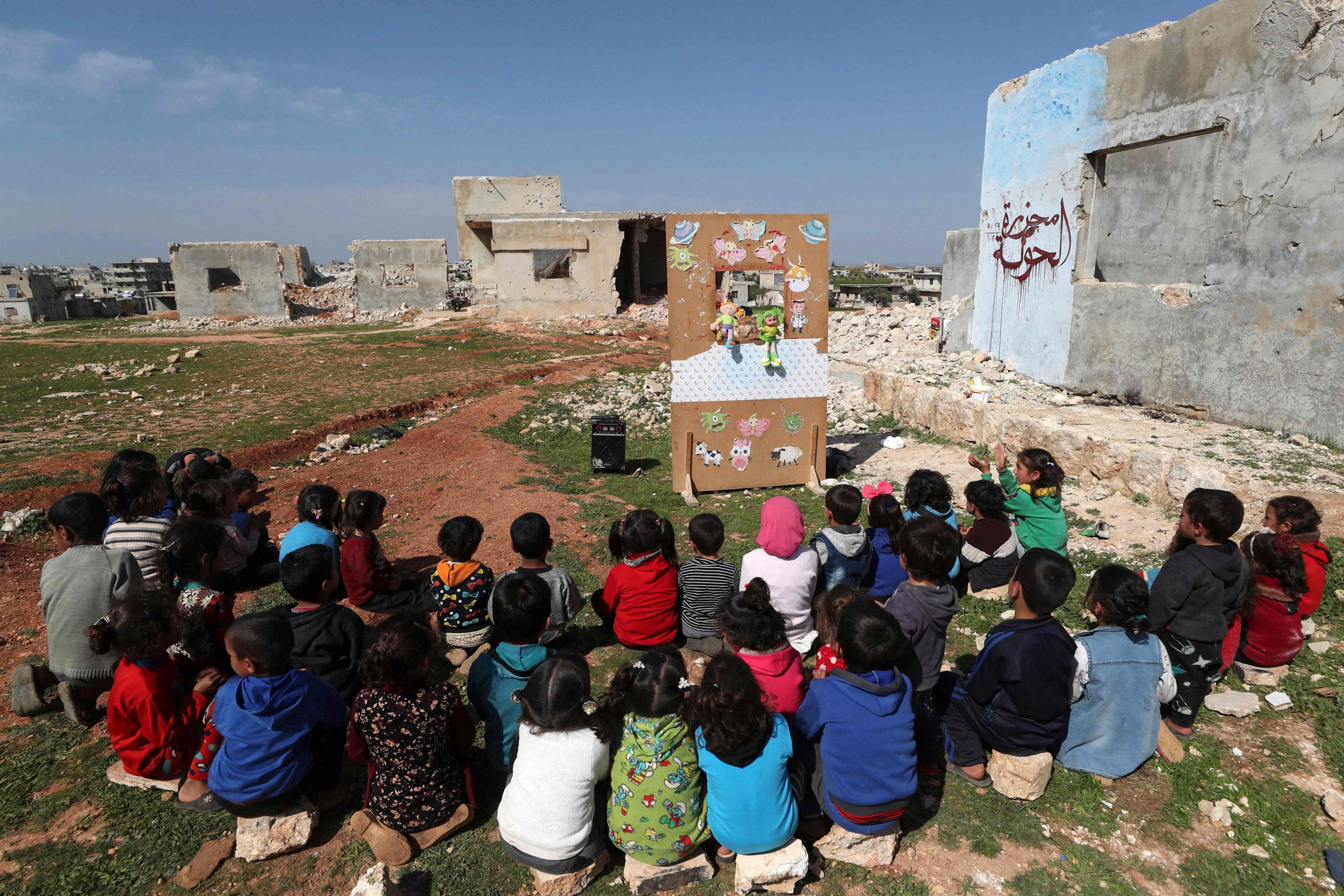 Syrian children watch a puppet show performed by a local theater group amid the ruins of buildings destroyed during Syria's civil war, in al-Fua, in the country's northwestern Idlib, Syria, March 30, 2021. (Photo by Omar Haj Kadour via AFP)