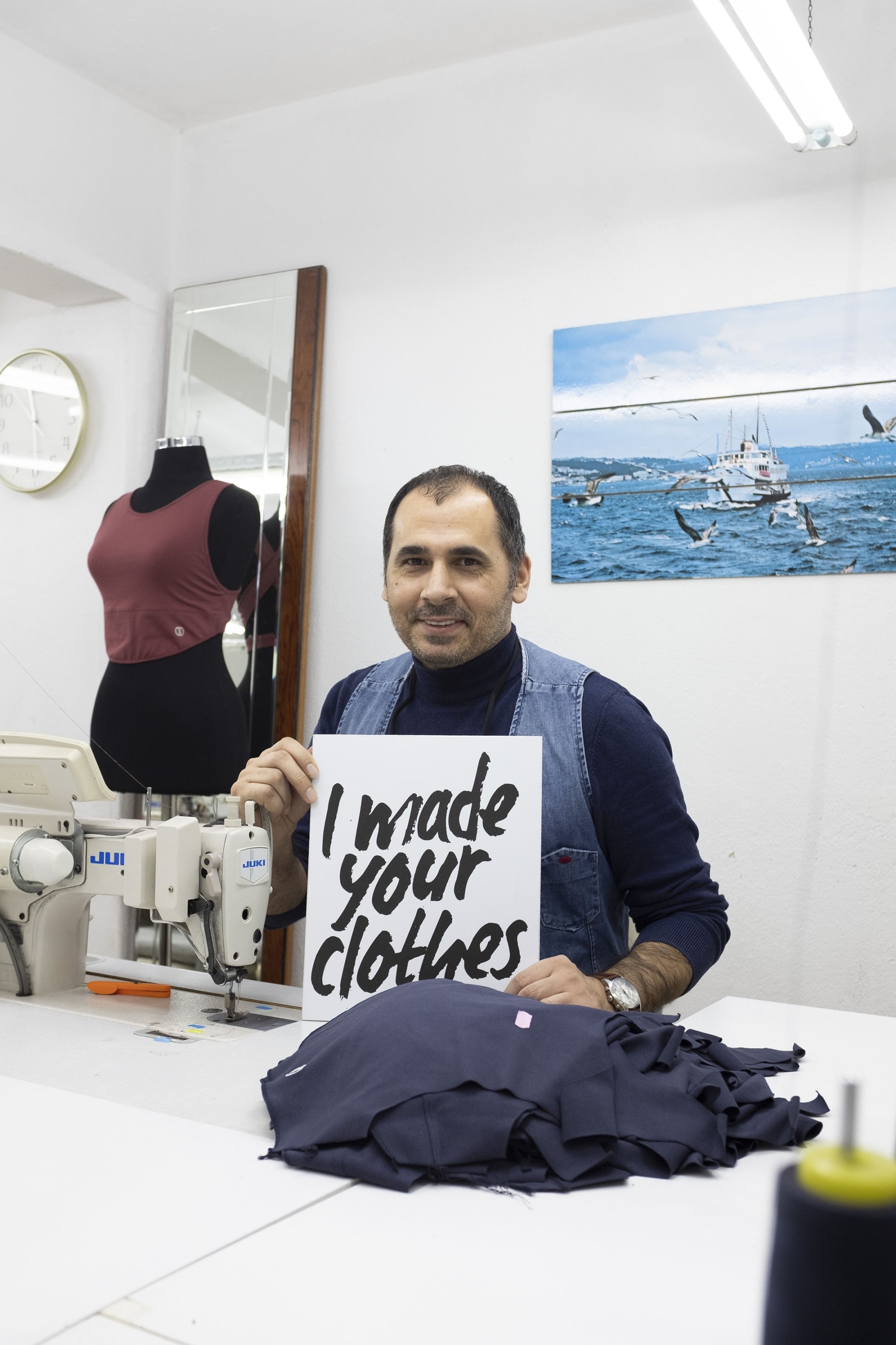 Master tailor Birol holds a sign that reads 'I made your clothes.' (Courtesy of Ezgi Utan)