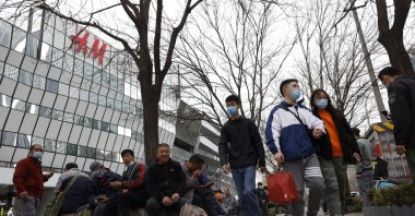 Visitors to a shopping mall wearing masks pass by an H&M store in Beijing, China, March 29, 2021. (AP Photo)