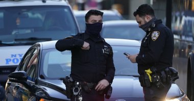 Police officers stand at the intersection of Main Street and Roosevelt Avenue as pedestrians pass them in the Flushing neighborhood of the Queens borough of New York, U.S., March 30, 2021. (AP Photo)
