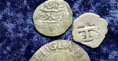 A 17th-century Arabian silver coin, top, that research shows was struck in 1693 in Yemen, rests near an Oak Tree Shilling minted in 1652 by the Massachusetts Bay Colony, below, and a Spanish half-real coin from 1727, right, on a table, in Warwick, Rhode Island, U.S., March 11, 2021. (AP Photo)