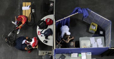 Riders take a break during a training session as a woman receives Pfizer's COVID-19 vaccine at the National Velodrome in Saint-Quentin-en-Yvelines, March 29, 2021. (AP Photo)