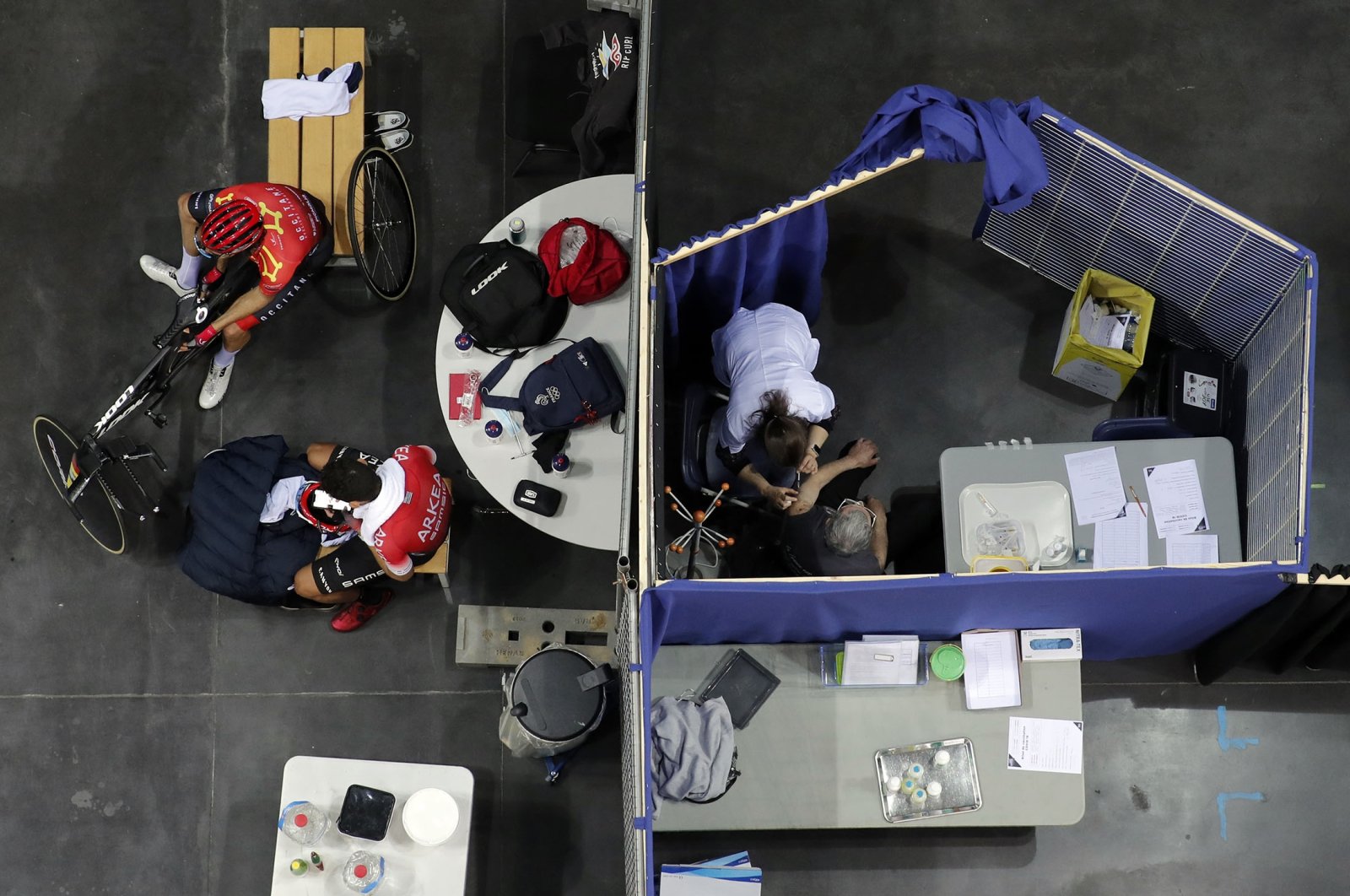 Riders take a break during a training session as a woman receives Pfizer's COVID-19 vaccine at the National Velodrome in Saint-Quentin-en-Yvelines, March 29, 2021. (AP Photo)