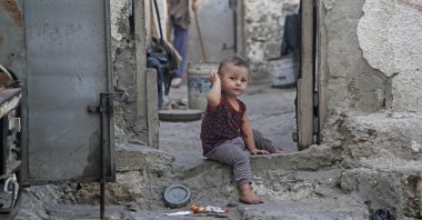 A toddler sits in a doorway of a deserted house as a woman sweeps at the Shati Palestinian refugee camp in Gaza City, Palestine, Sept. 3, 2019. (AFP Photo)