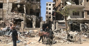 People stand in front of damaged buildings, in the town of Douma, the site of a chemical weapons attack, near Damascus, Syria, Monday, April 16, 2018. (AP Photo/Hassan Ammar)