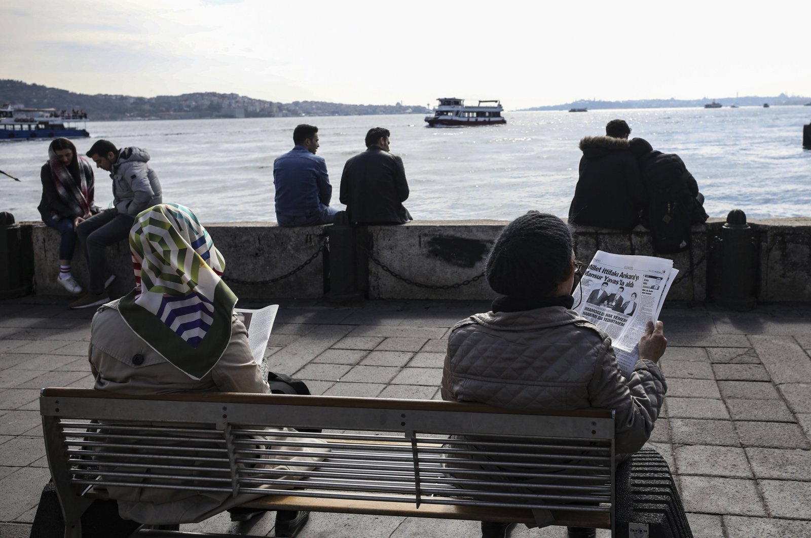 People sit reading newspapers that contain information regarding local elections a day after the vote, next to the Bosporus in Istanbul, Turkey, April 1, 2019. (AP Photo)