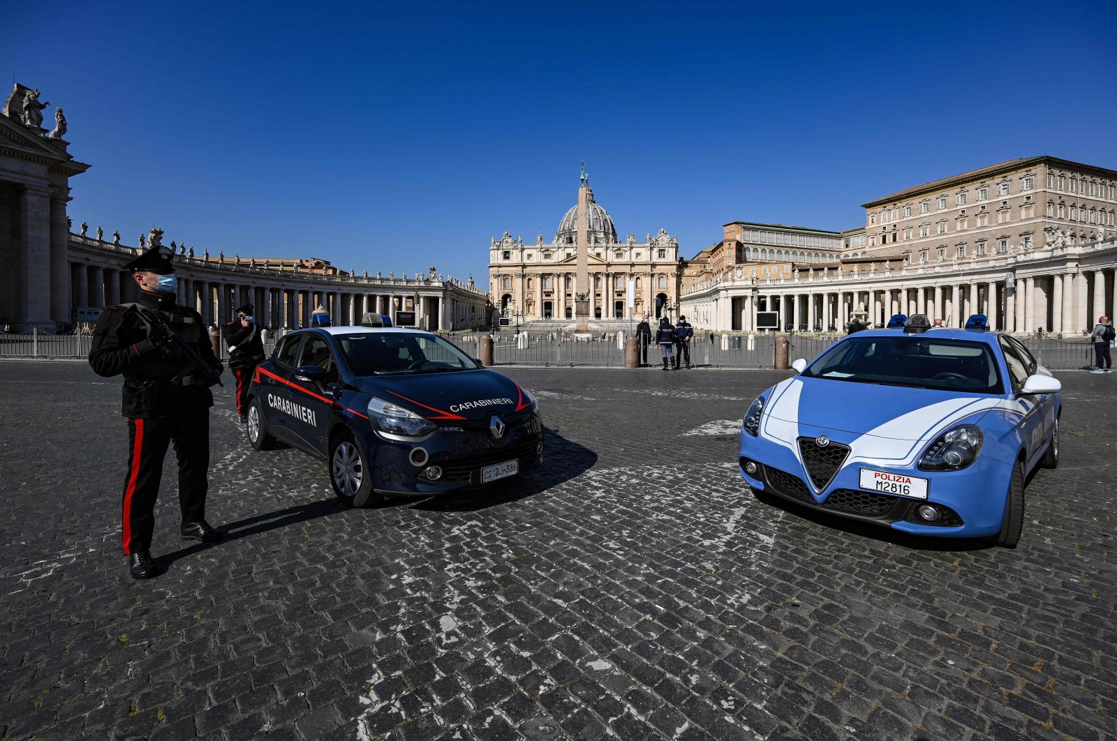 An Italian Carabinieri Police officer (L) stands guard at the limit between Italy in Rome and Saint Peter's Square in The Vatican, with Saint Peter's Basilica in the background, in The Vatican, March 28, 2021. (AFP Photo)