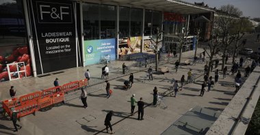 People observe social distancing in an attempt to stop the spread of the coronavirus by standing behind tape lines as they line up to shop outside a branch of the Tesco supermarket chain in west London, U.K., April 10, 2020. (AP Photo)