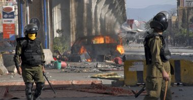 Police officers walk past a burning van set on fire by angry supporters of Tehreek-e-Labiak Pakistan (TLP), a radical political party, during a clash, in Rawalpindi, Pakistan, April 14, 2021. (AP Photo)