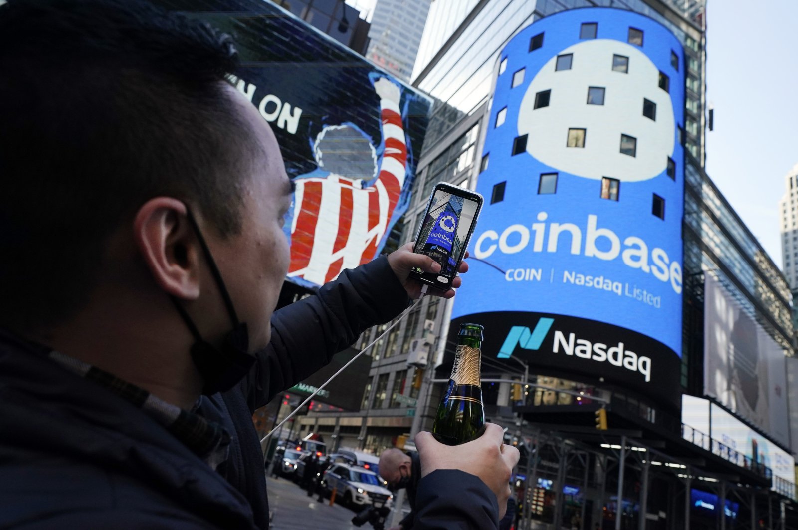 Coinbase employee Daniel Huynh holds a celebratory bottle of champagne as he takes a photograph outside the Nasdaq MarketSite, in Times Square, New York, U.S., Wednesday, April 14, 2021. (AP Photo)