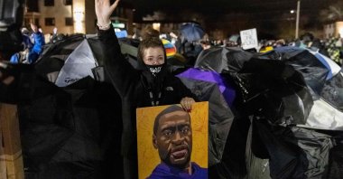 A demonstrator holding a poster of George Floyd, raises her hand toward a line of police officers outside the Brooklyn Center police station while protesting the death of Daunte Wright who was shot and killed by a police officer in Brooklyn Center, Minnesota, April 14, 2021. (AFP Photo)