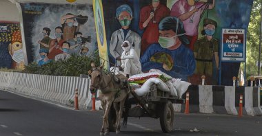 A man rides a horse cart past a mural depicting frontline workers in Noida, a suburb of New Delhi, India, Thursday, April 15, 2021. (AP Photo)