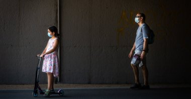 A little girl wearing a protective face mask rides an electric scooter as her father walks behind her through Madrid Rio Park amid the coronavirus outbreak, Madrid, Spain, May 25, 2020. (Photo by Getty Images)