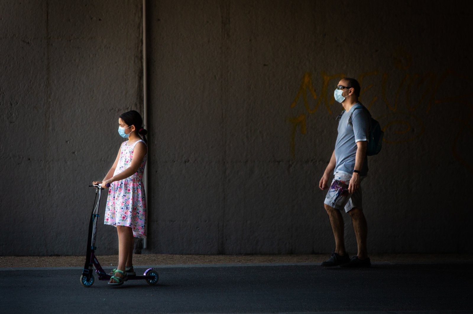 A little girl wearing a protective face mask rides an electric scooter as her father walks behind her through Madrid Rio Park amid the coronavirus outbreak, Madrid, Spain, May 25, 2020. (Photo by Getty Images)