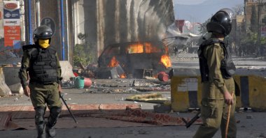 Police officers walk past a burning van setting on fire by angry supporters of Tehreek-e-Labiak Pakistan, a radical Islamist political party, during a clash, in Rawalpindi, Pakistan, April 14, 2021. (AP Photo)