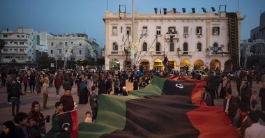 People carry a giant Libyan flag at the Martyrs square during a march commemorating the anniversary of anti-Gadhafi protests in Tripoli, Libya, Feb. 25, 2020. (AP Photo)