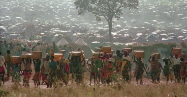 Refugees who fled the ethnic bloodbath in neighboring Rwanda carry water containers back to their huts at the Benaco refugee camp in Tanzania, near the border with Rwanda, May 17, 1994. (AP Photo)