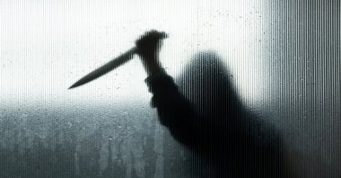 Blurred shadow of hand holding knife behind frosted glass in the bathroom. (Shutterstock Photo)