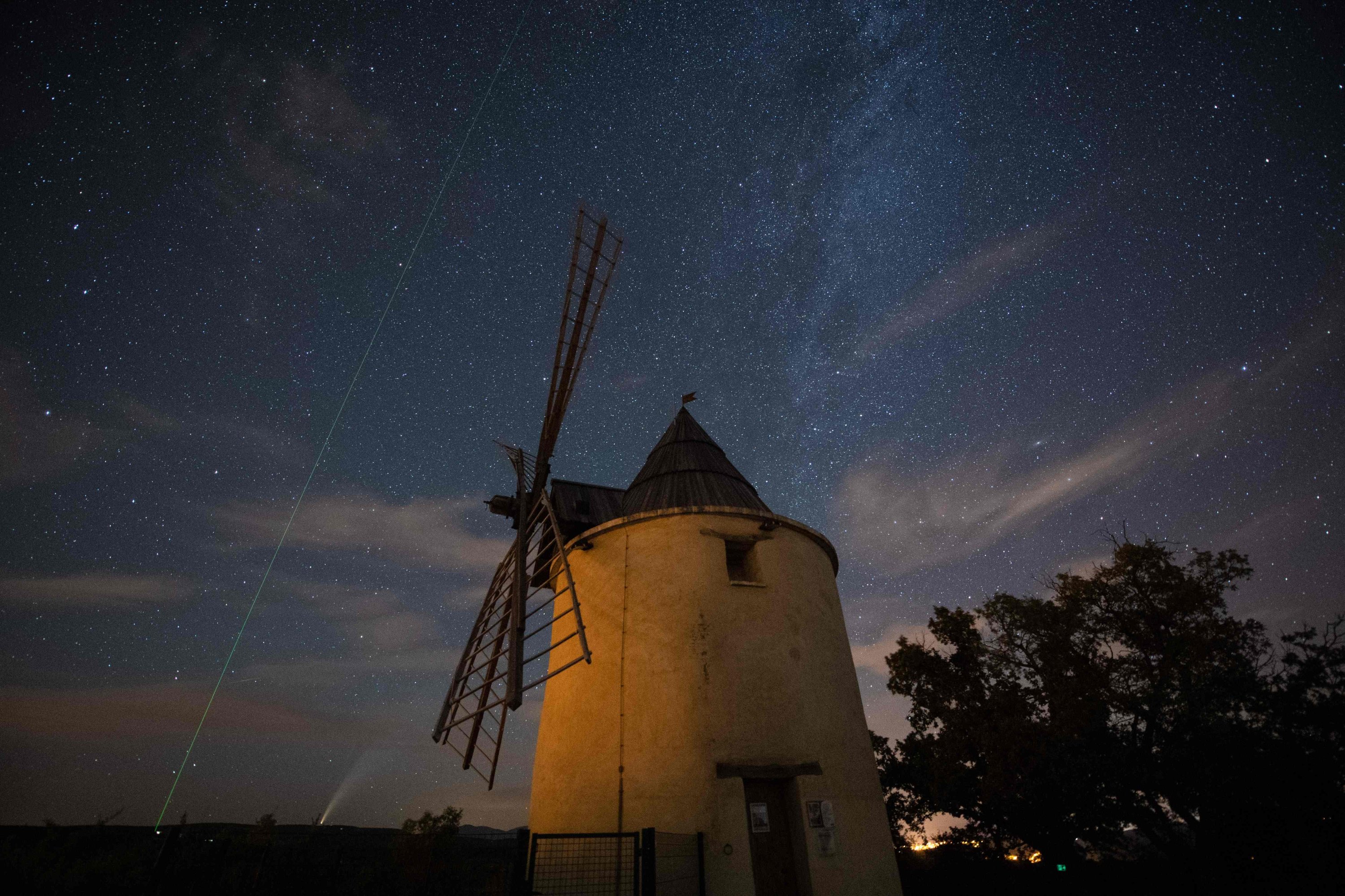 A picture taken on July 15, 2020 shows the C/2020 F3 comet (C), also known as "NEOWISE", the green laser beam used by the Haute-Provence Observatory to point celestial objects for studies and researches (L) and the Milky Way (R), with an old windmill in the foreground in Saint-Michel-L