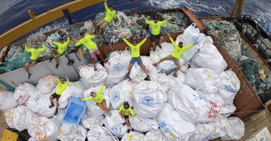 Workers with the Papahanaumokuakea Marine Debris Project pose on top of fishing nets and plastics collected from the the beaches of the Northwestern Hawaiian Islands, Hawaii, April 21, 2021. (Papahanaumokuakea Marine Debris Project via AP)