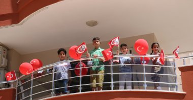 Children confined to home due to pandemic, wave flags and balloons at the balcony of their home, in Alanya district, in Antalya, southern Turkey, Apr. 23, 2021. (İHA PHOTO) 