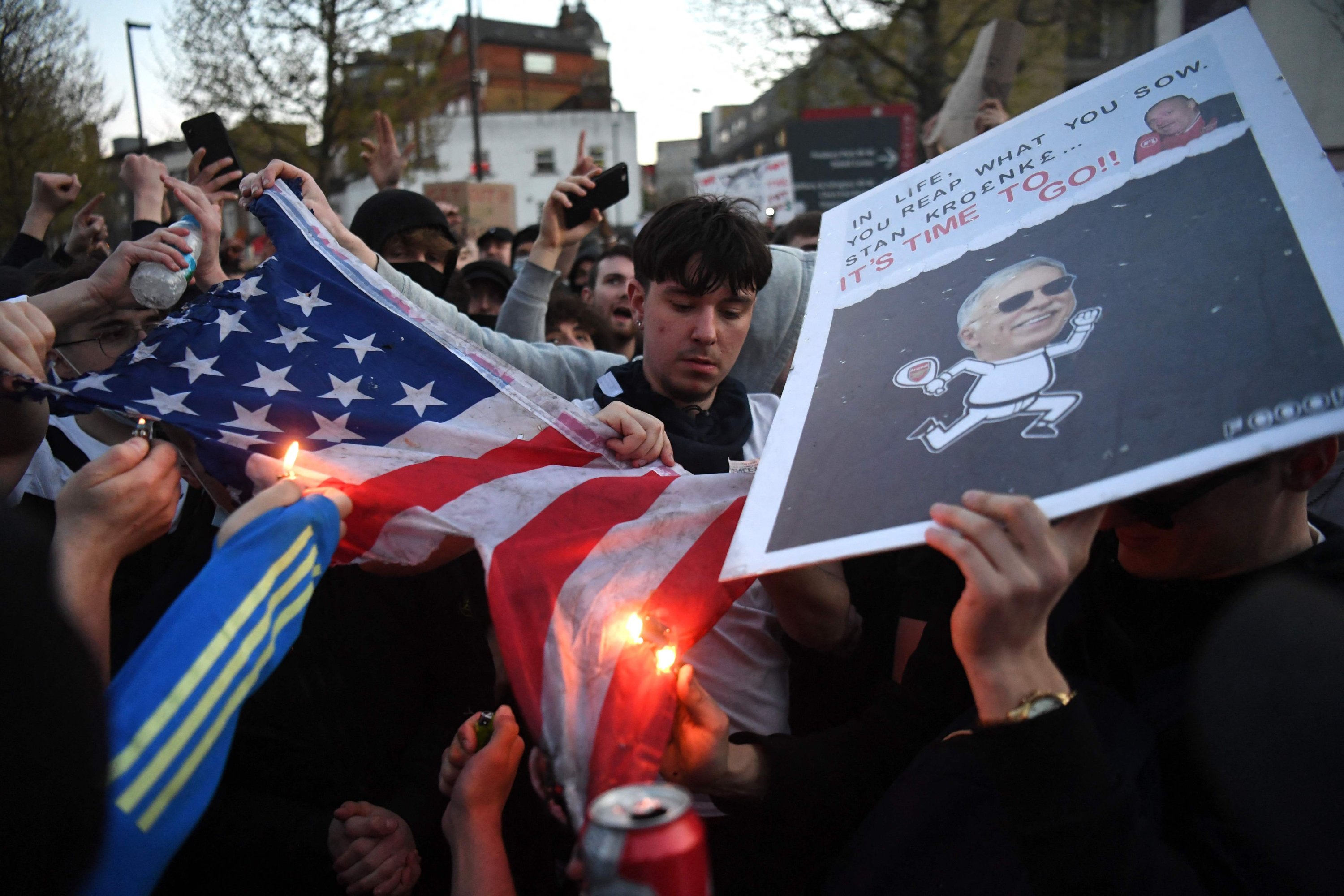 Supporters try to set alight a U.S. flag as they protest against Arsenal's U.S. owner Stan Kroenke ahead of their game against Everton, outside English Premier League club Arsenal's Emirates stadium in London, Britain, April 23, 2021. (AFP)