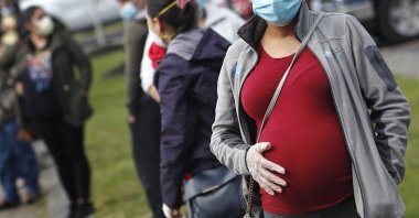 In this May 7, 2020 file photo, a pregnant woman wearing a face mask and gloves holds her belly as she waits in line for groceries at St. Mary's Church in Waltham, Massachusetts, U.S. (AP Photo)