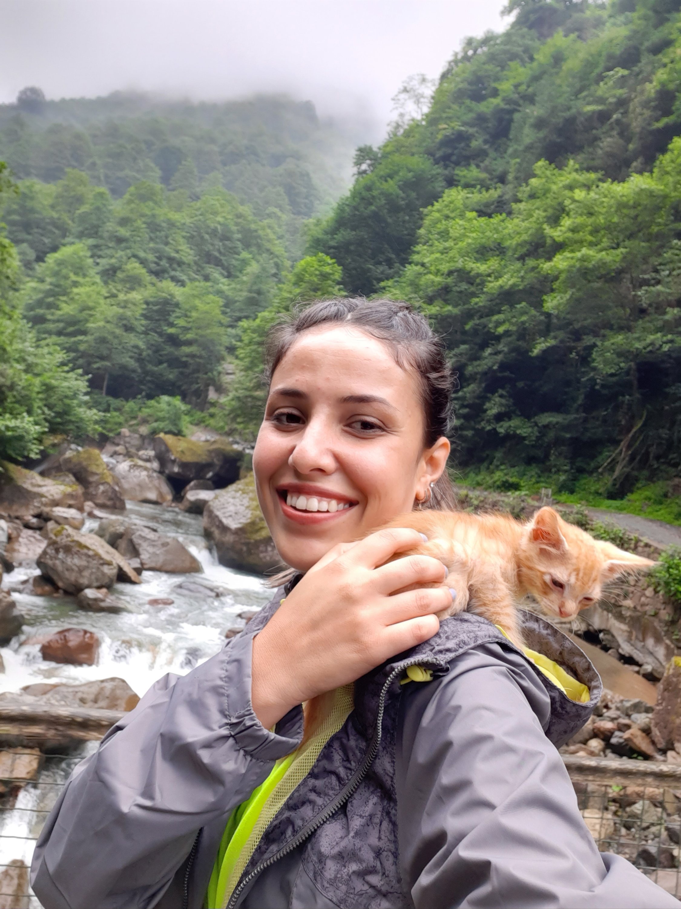 Özge Kübra Teymur poses for a photo with her cat Azman resting on her shoulder against a backdrop of forests and mountains, Rize, Turkey, April 20, 2021. (DHA Photo)