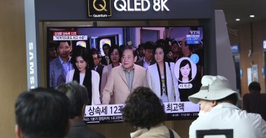 People watch a TV screen showing a file image of the late Samsung Electronics chairperson Lee Kun-Hee (C) and his daughters during a news program at Seoul Railway Station in Seoul, South Korea, April 28, 2021. (AP Photo)