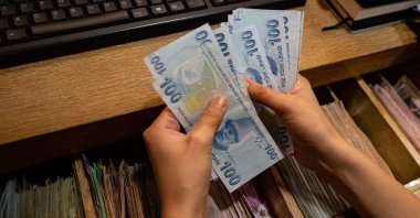 A currency exchange office worker counts Turkish lira banknotes in front of the electronic panel displaying currency exchange rates at an exchange office in Istanbul, Turkey, Aug. 6, 2020. (AFP Photo)