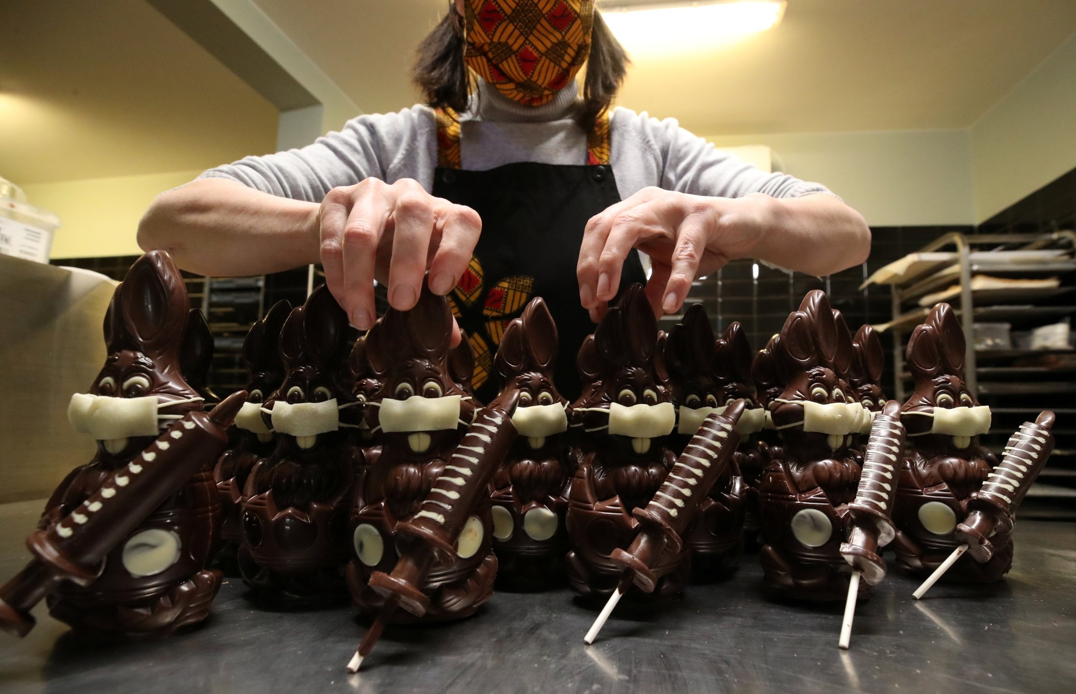 Belgian artisan chocolate maker Genevieve Trepant works on her chocolate bunnies wearing protective masks and holding vaccine syringes called "L