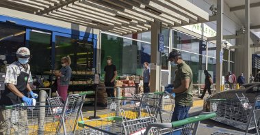 Whole Foods Market 365 supermarket workers wear masks and gloves as they sanitize shopping carts, while shoppers wait in line to enter the store, observing social distancing during the coronavirus pandemic, Los Angeles, the U.S., April 17, 2020. (AP File Photo)