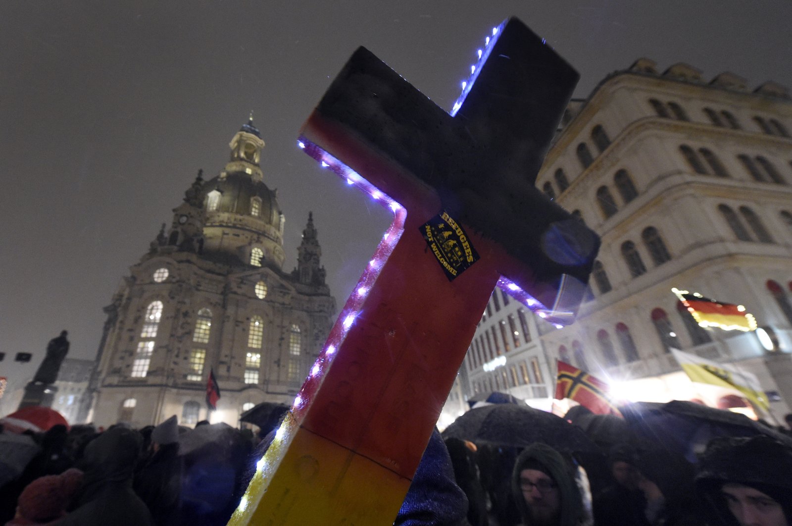 An illuminated cross with a sticker reading "refugees not welcome" is pictured during a demonstration of PEGIDA close to the Frauenkirche church in Dresden, eastern Germany, Feb. 29, 2016. (AP Photo)