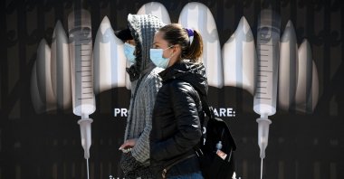 People wearing protective masks walk by a banner showing syringes as vampire fangs during the vaccination marathon organized at Bran Castle in Bran village, Romania, May 8, 2021. (AFP Photo)
