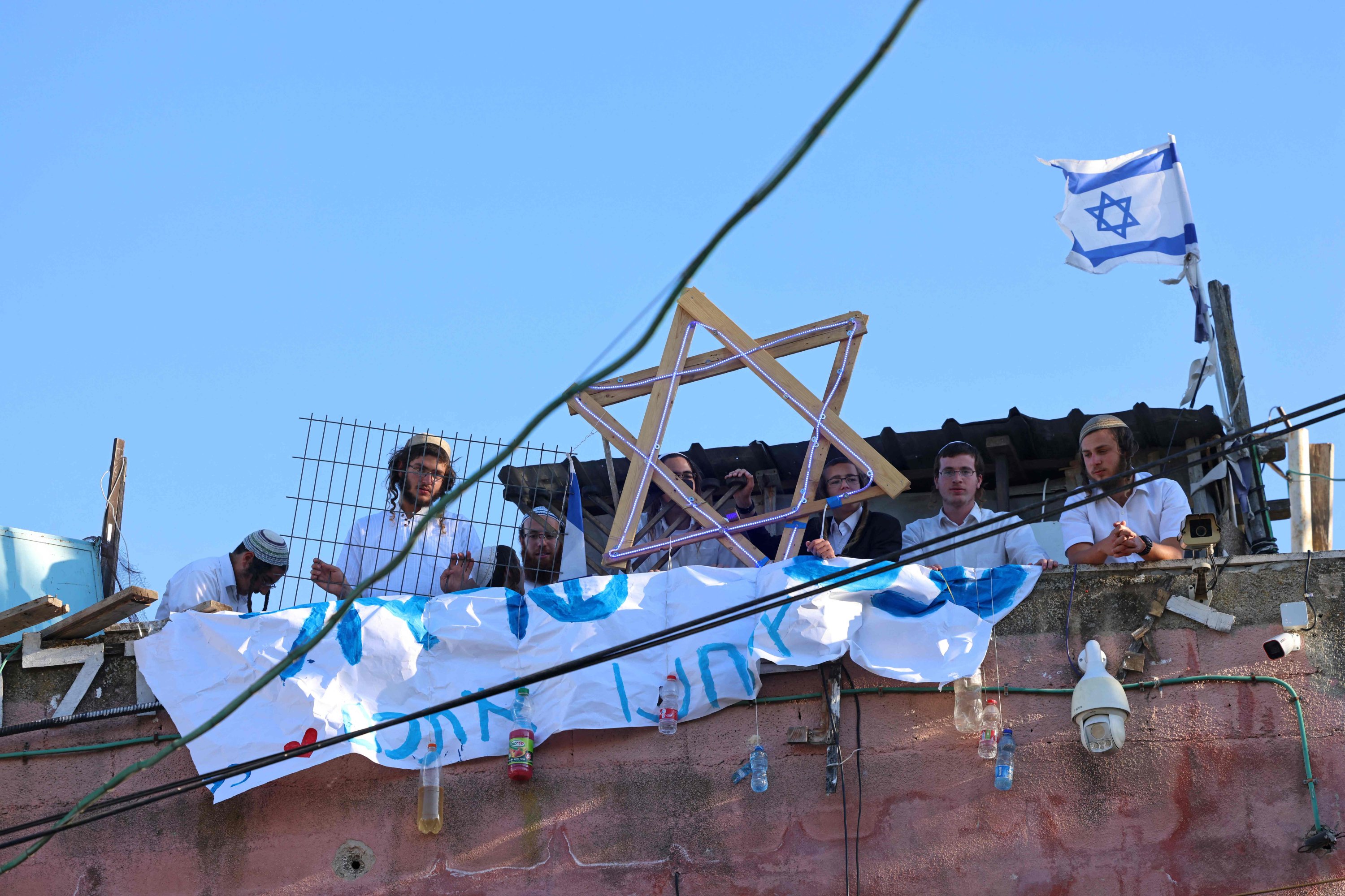 Israeli settlers sit on the rooftop of a house decorated with the Star of David in the Sheikh Jarrah neighbourhood of East Jerusalem, occupied Palestine, on May 15, 2021. (AFP Photo)
