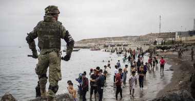 People mainly from Morocco stand on the shore as Spanish Army cordon off the area at the border of Morocco and Spain, at the Spanish enclave of Ceuta, on Tuesday, May 18, 2021. (AP Photo)