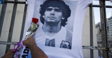 A man places a flower on a jersey with the face of late footballing icon Diego Maradona during a march to demand answers regarding his death, in Buenos Aires, Argentina, March 10, 2021. (AP Photo)