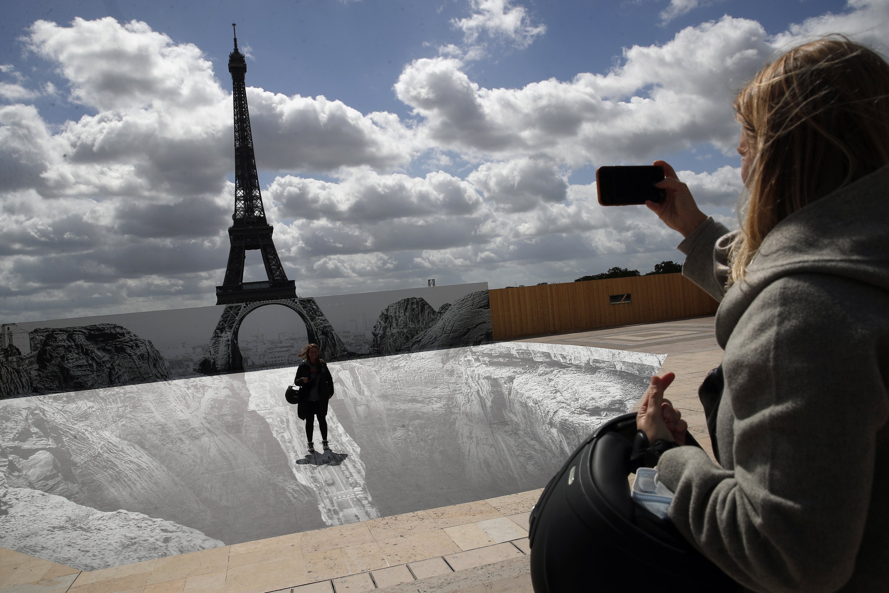 A woman takes a photo of her friend on the Trocadero square in front of the Eiffel Tower where French artist and photographer JR set his artwork, in Paris, France, May 21, 2021. (AP Photo)