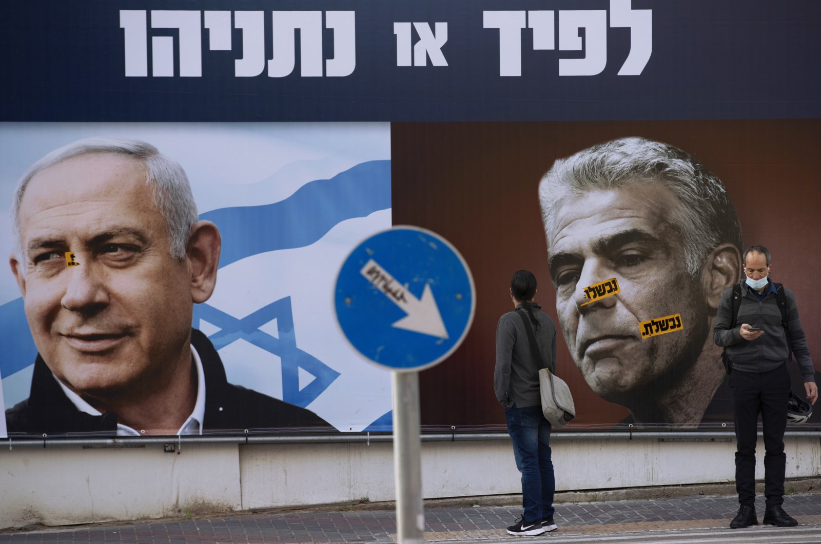 People stand in front of an election campaign billboard for the Likud party showing a portrait of its leader Prime Minister Benjamin Netanyahu (L) and opposition party leader Yair Lapid, in Ramat Gan, Israel, March 14, 2021. (AP Photo)